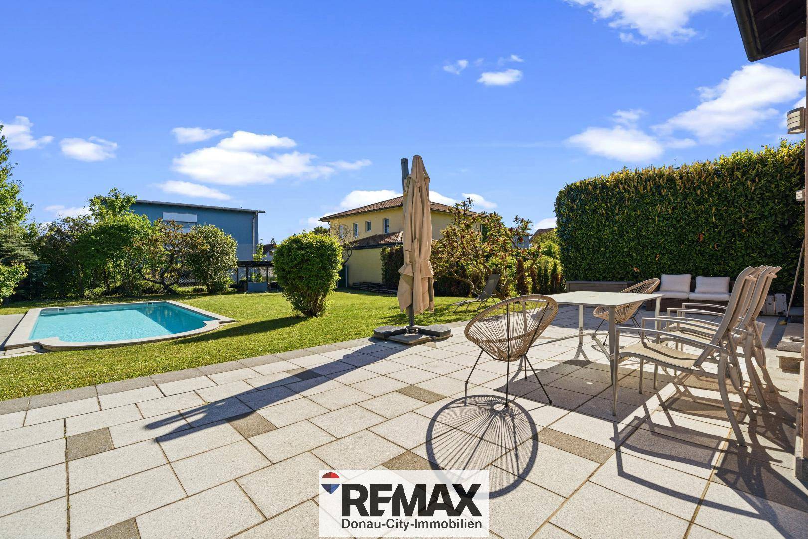 Große gepflasterte Terrasse mit Sitzgelegenheiten und Blick auf den Garten und Pool.