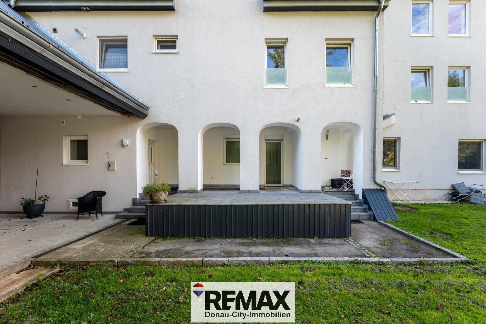 Hintere Terrasse mit Arkaden und Zugang zum kleinen Rasenbereich, ideal für Entspannung im Freien.