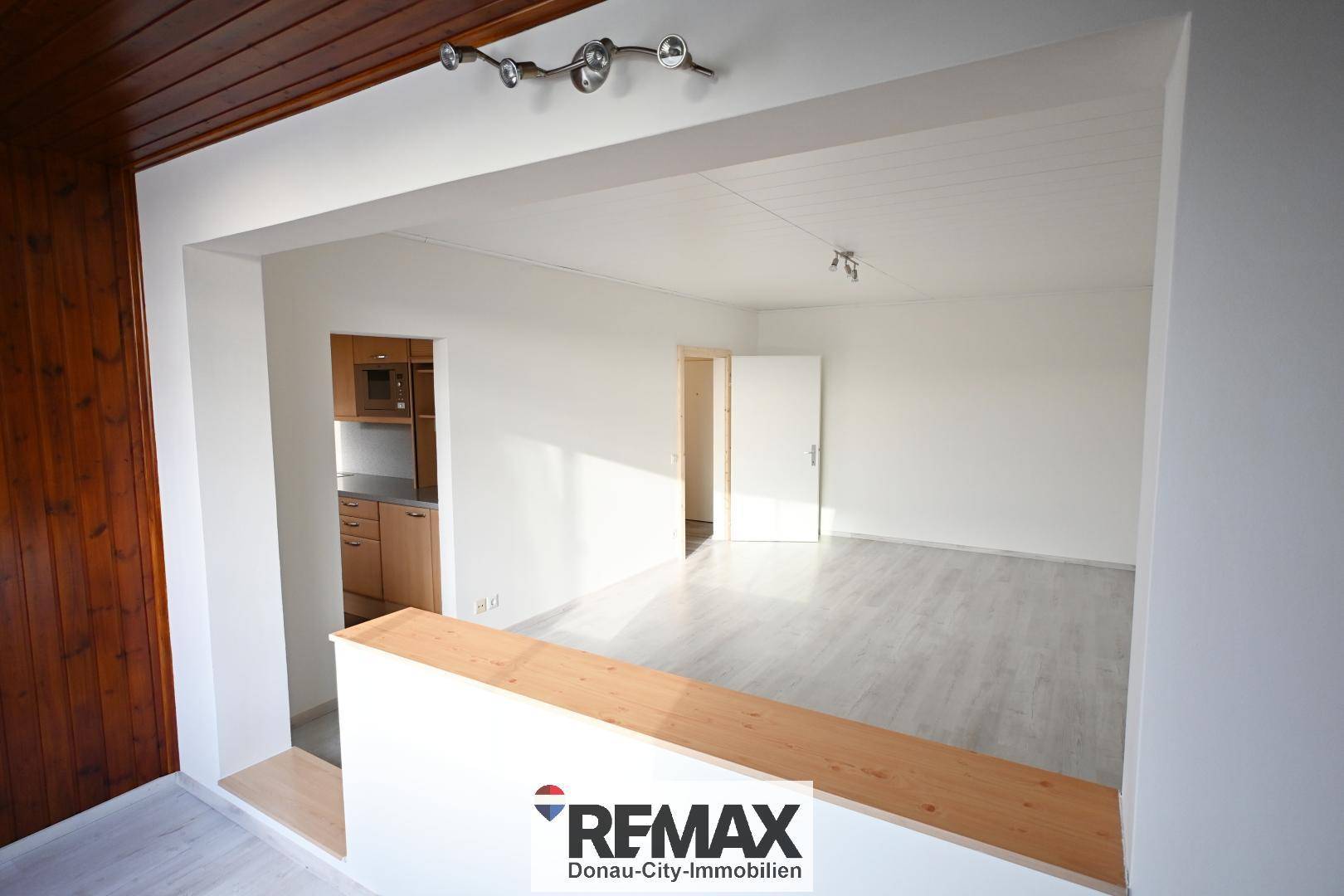 Geräumiger Wohnbereich mit hellem Laminatboden und Holzakzenten an der Decke und Wand.