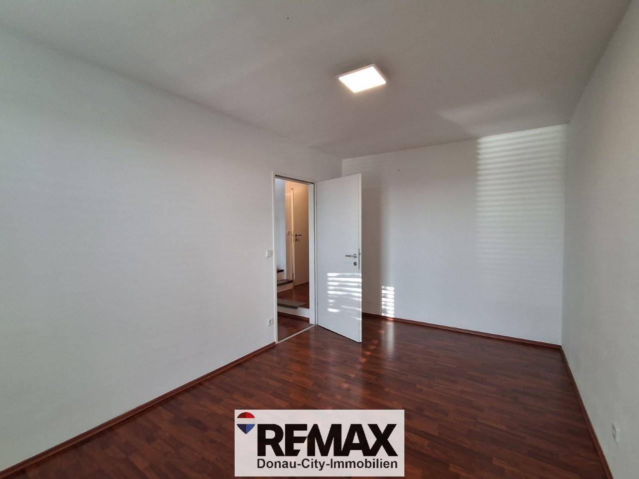 Leeres Zimmer mit dunklem Laminatboden und weißen Wänden, bereit zur individuellen Gestaltung.