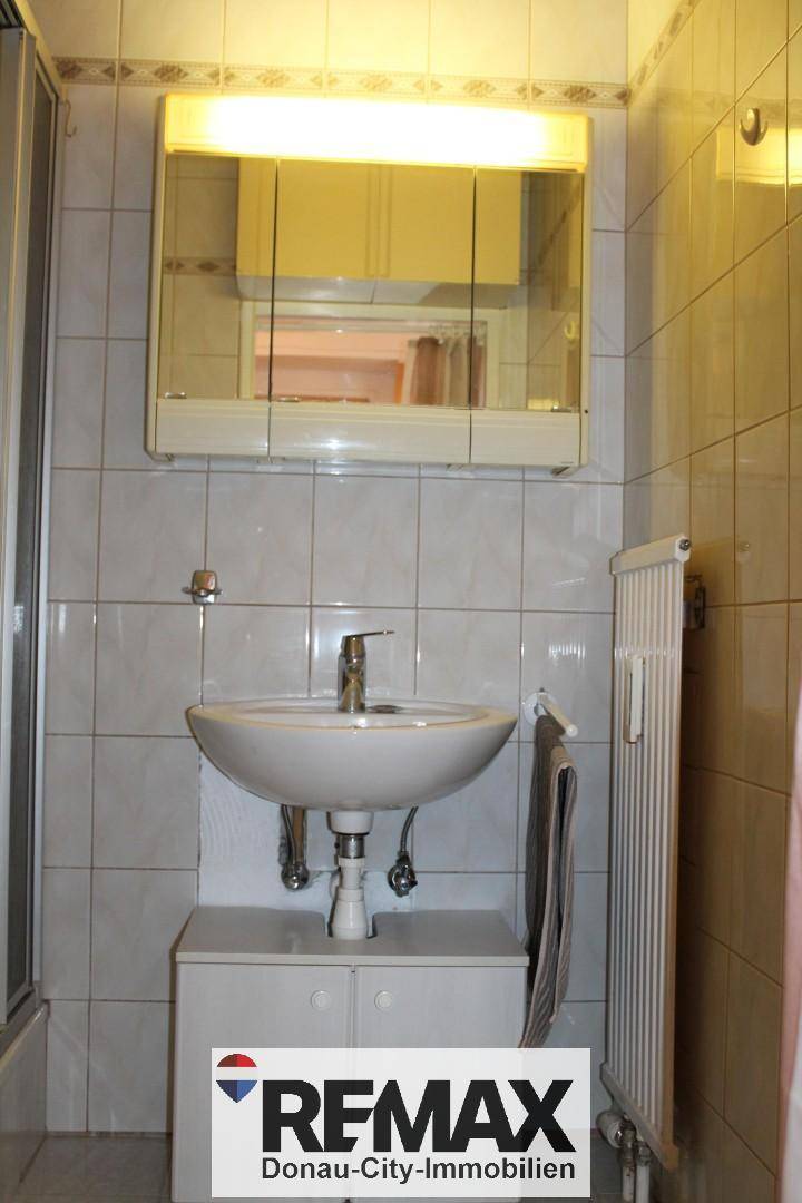 Badezimmer mit Waschbecken, Spiegelschrank und hellen Wandfliesen.