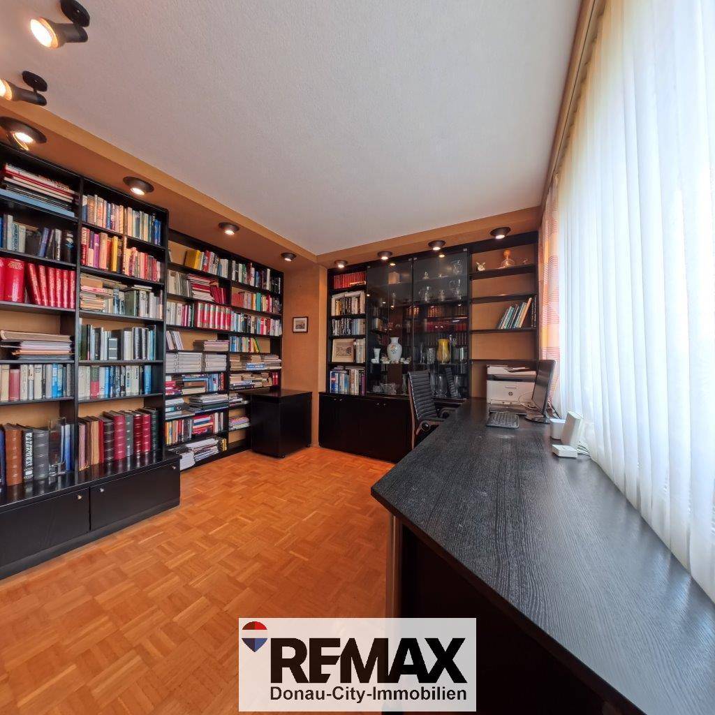 Arbeitszimmer mit raumhohen Bücherregalen, Schreibtisch und Parkettboden.