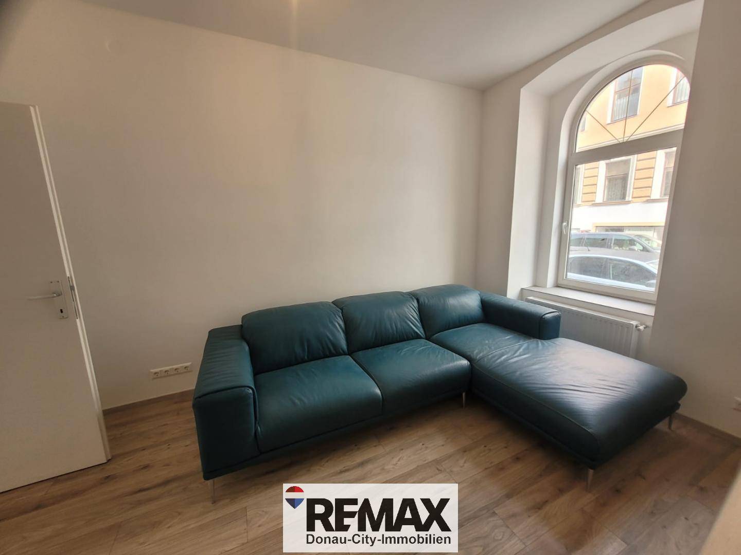 Gemütliches Wohnzimmer mit einem großen Ecksofa und einem Bogenfenster zur Straße.