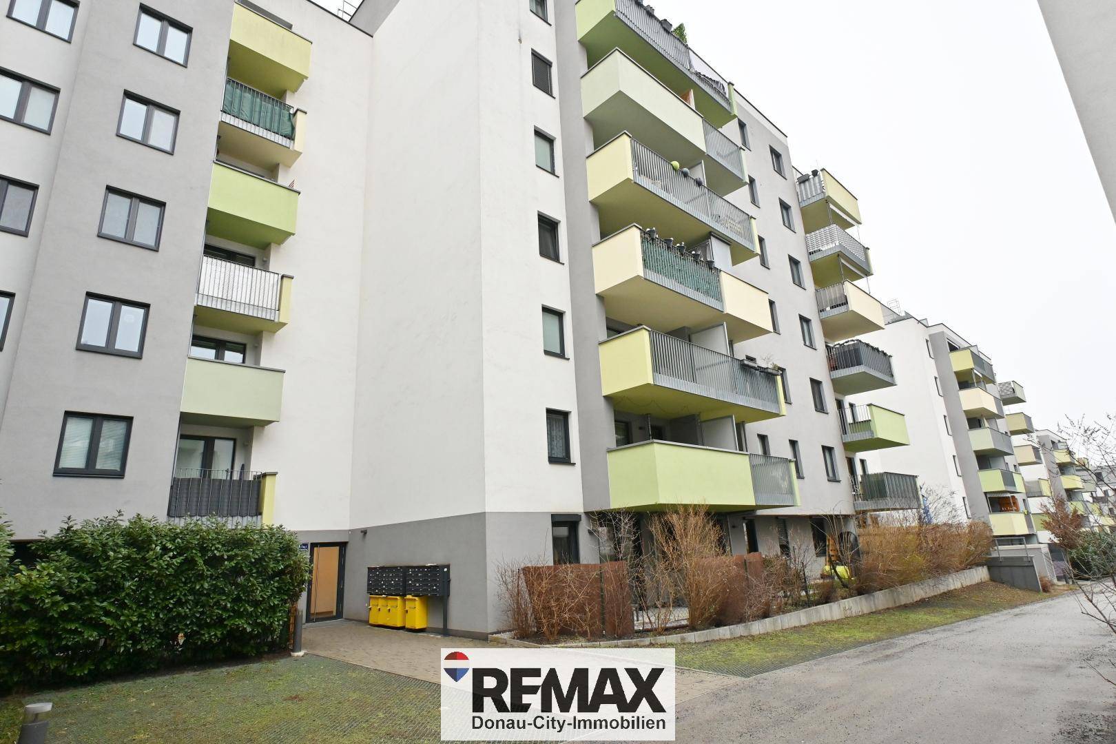 Modernes Mehrfamilienhaus mit farbigen Balkonen in Grüntönen und einer grauen Fassade.
