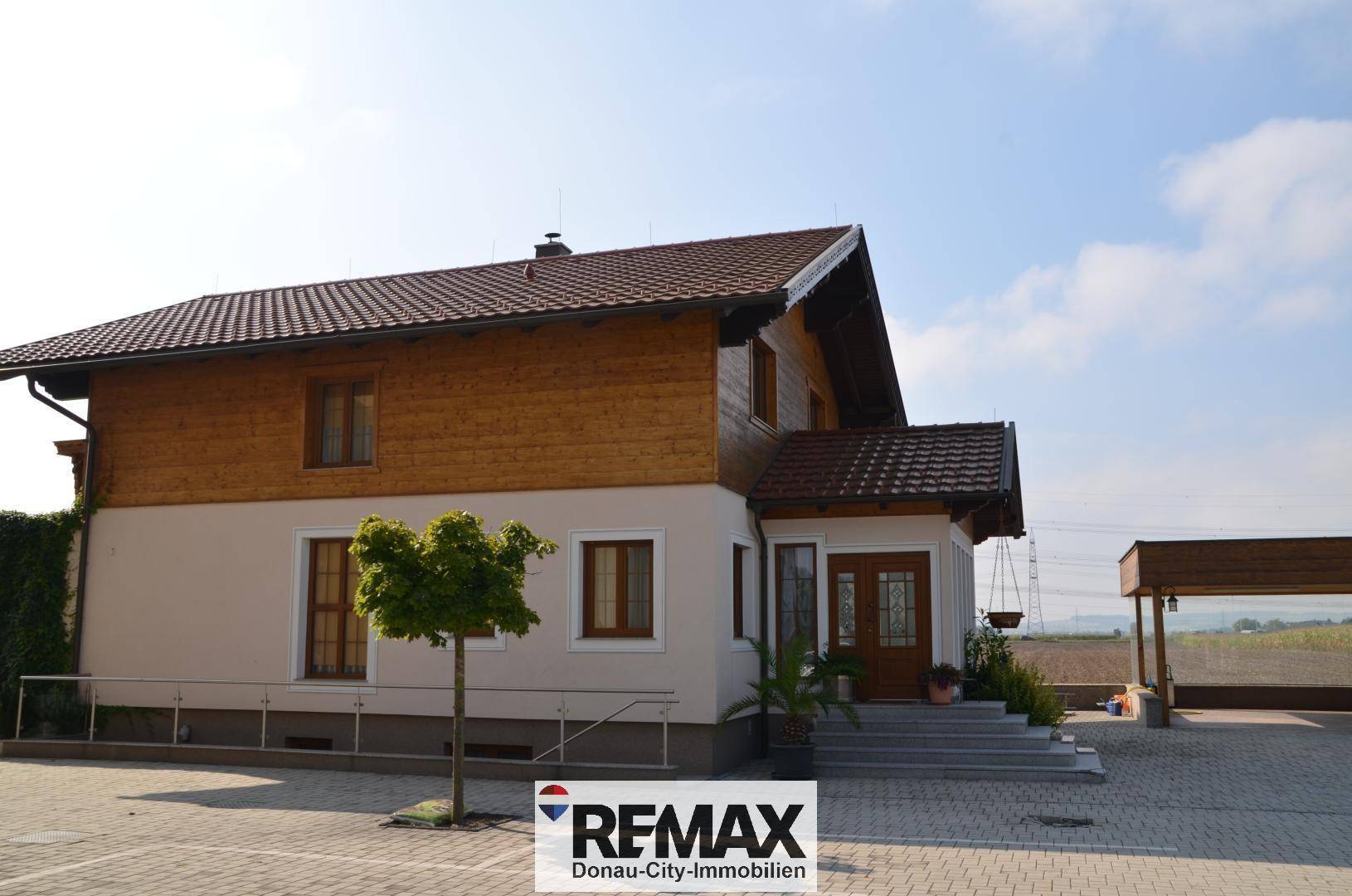 Ansicht des Hauses mit Holzfassade und gepflastertem Vorplatz unter klarem Himmel.