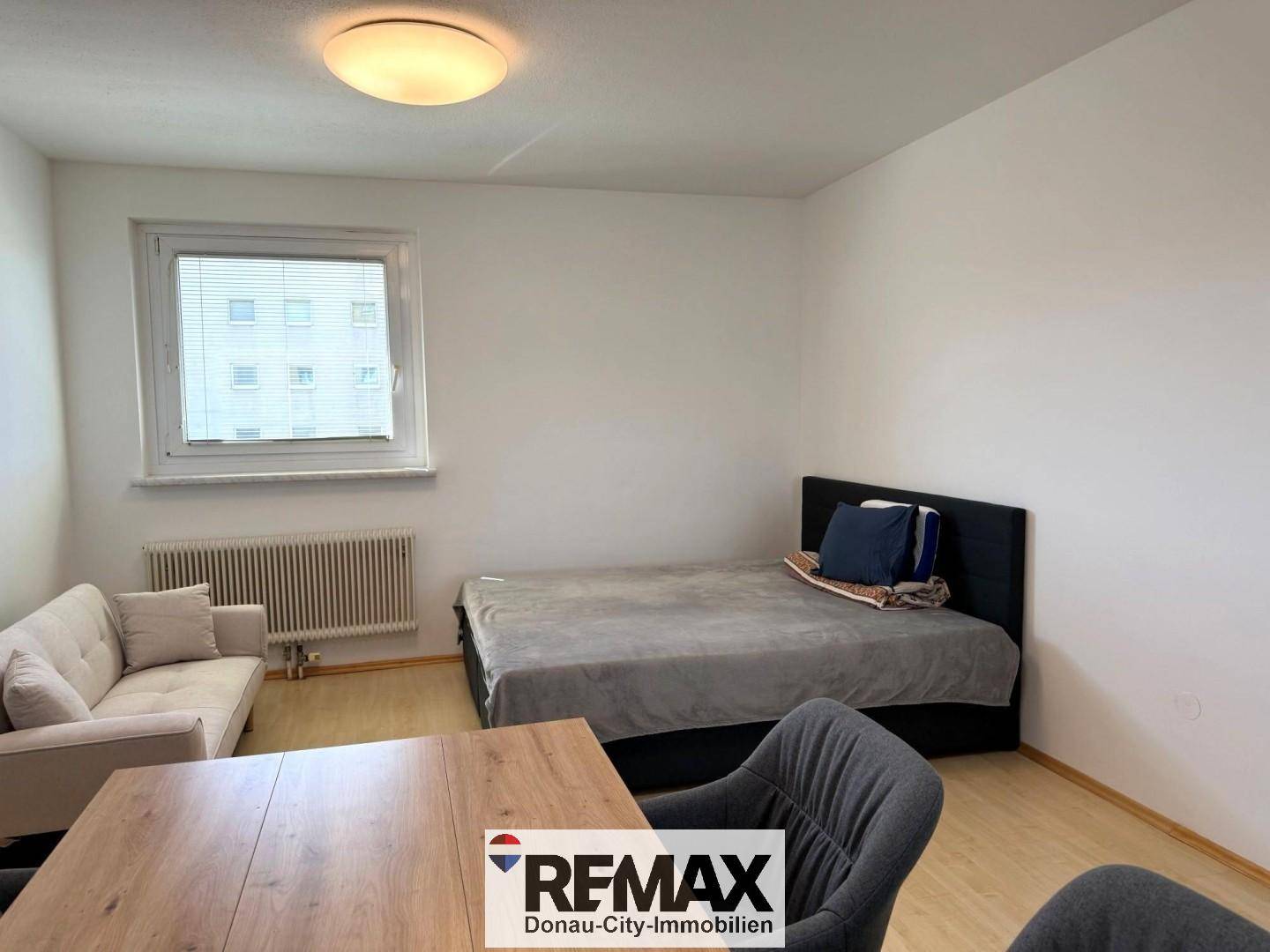 Heller Wohnraum mit Sofa, Tisch und Bett, ausgestattet mit Laminatboden.