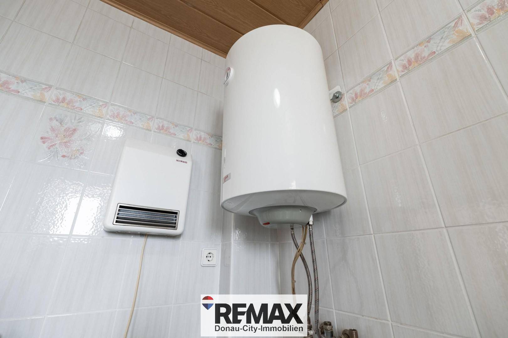 Nahaufnahme eines Warmwasserboilers und einer Wandheizung in einem gefliesten Raum.