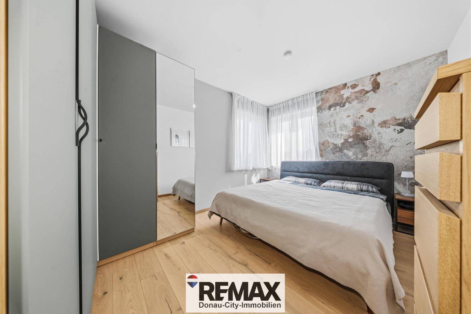 Gemütliches Schlafzimmer mit Doppelbett, Holzschrank und einer Akzentwand in Erdtönen.