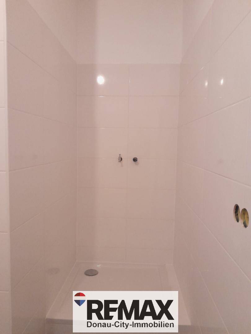 Duschbereich mit weißen Wandfliesen und einer flachen Duschwanne in einem modernen Badezimmer.