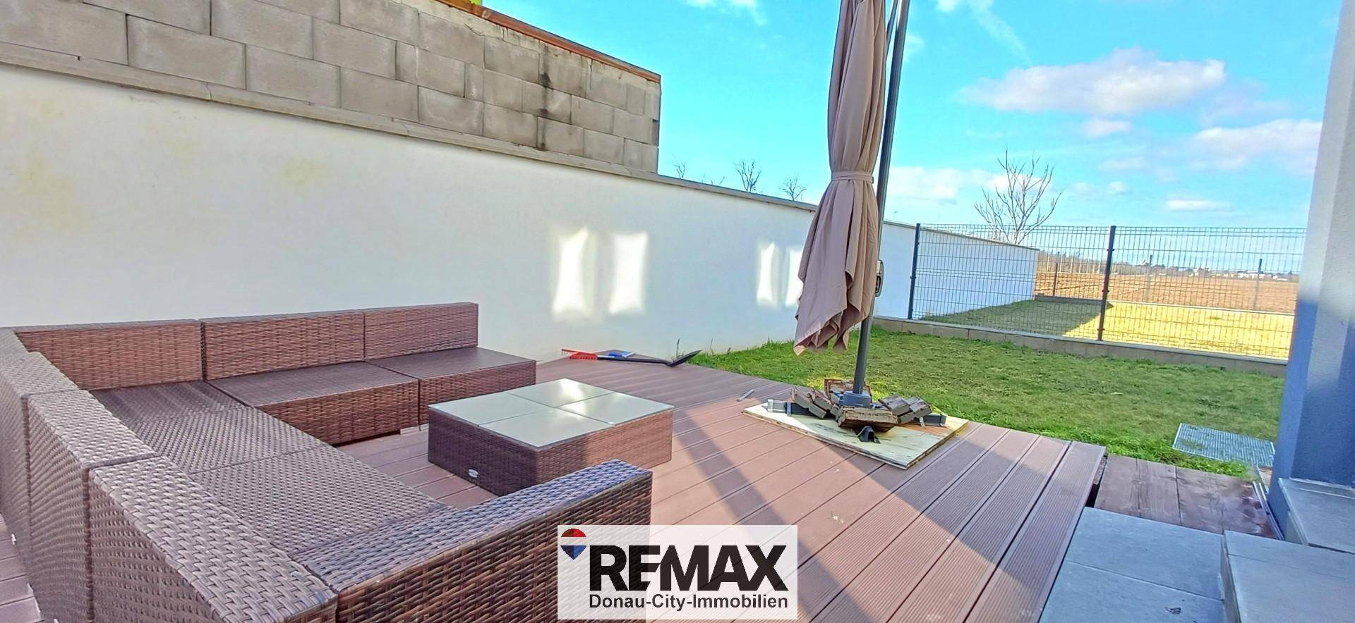 Terrasse mit Outdoor-Sitzbereich, Sonnenschirm und Rasenfläche.