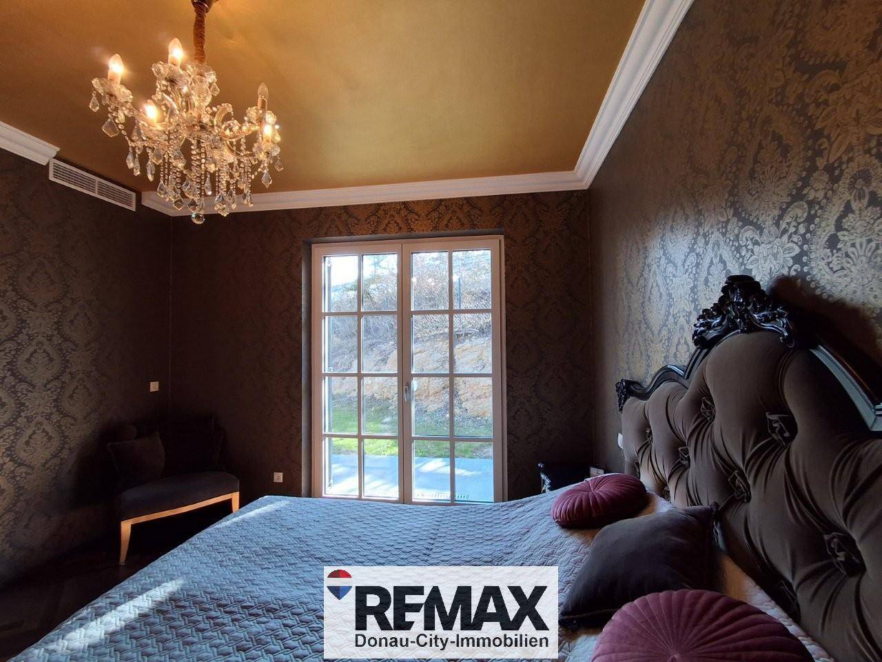 Elegantes Schlafzimmer mit opulentem Bett, gemusterter Tapete und großem Fenster.