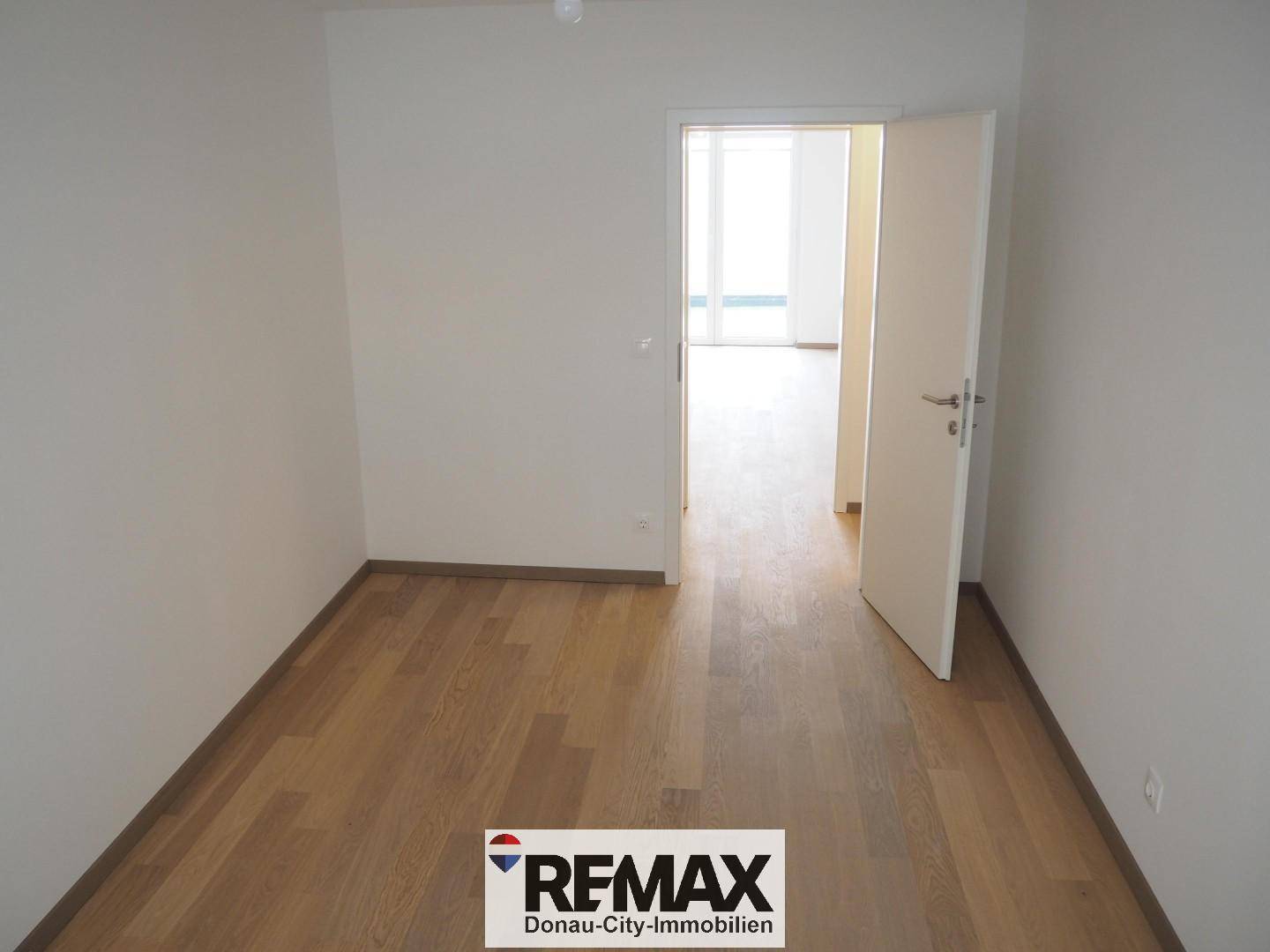 Schlafzimmer mit Holzboden und offener Tür zu einem weiteren hellen Raum.
