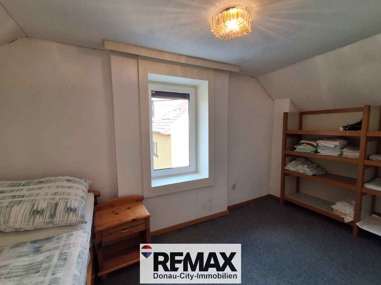 Dachgeschoss-Schlafzimmer mit Einzelbett, Holzregalen und Fenster, das Tageslicht spendet.