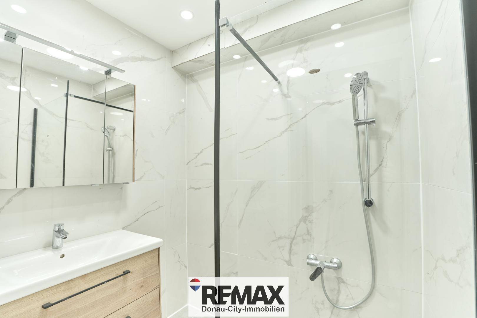 Modernes Badezimmer mit begehbarer Dusche, Einzelwaschbecken und eleganten Marmorfliesen.