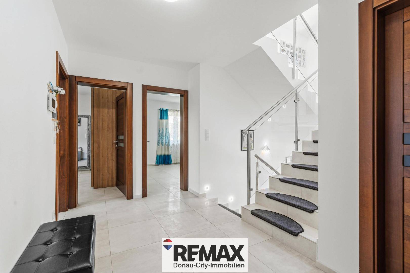 Heller Flur mit moderner Treppe aus Glas und Edelstahl, die in die obere Etage führt.