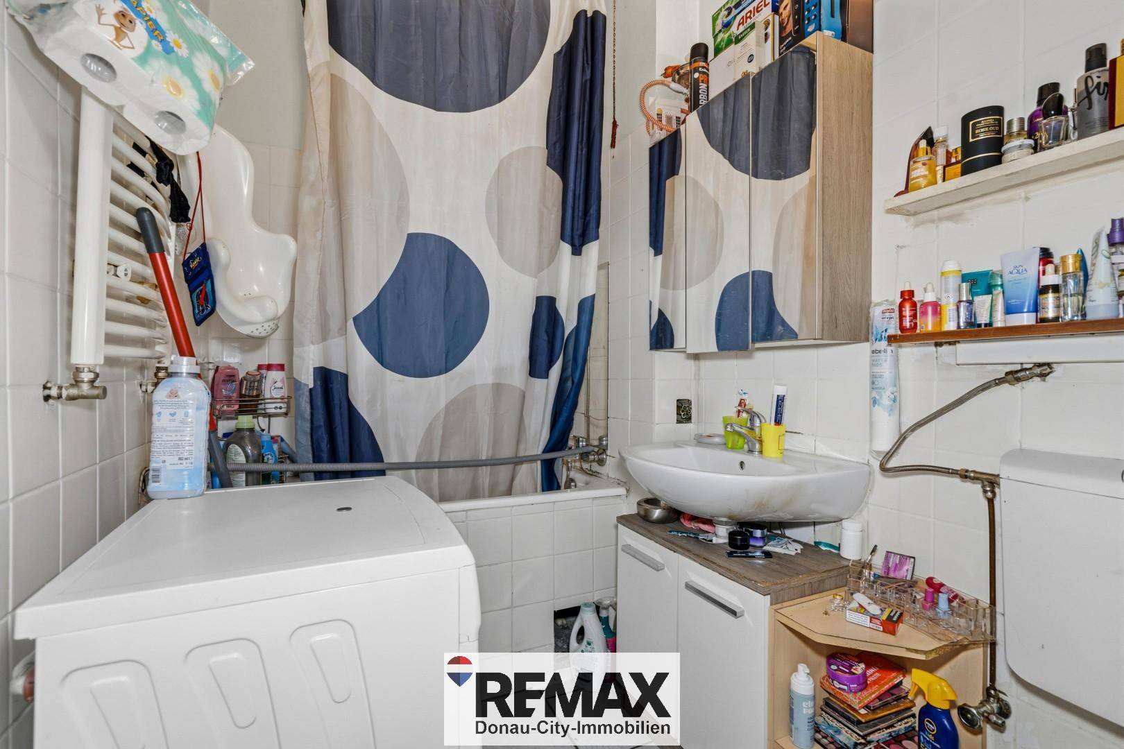 Badezimmer mit Badewanne, Waschbecken, Toilette und Waschmaschine, komplett gefliest.