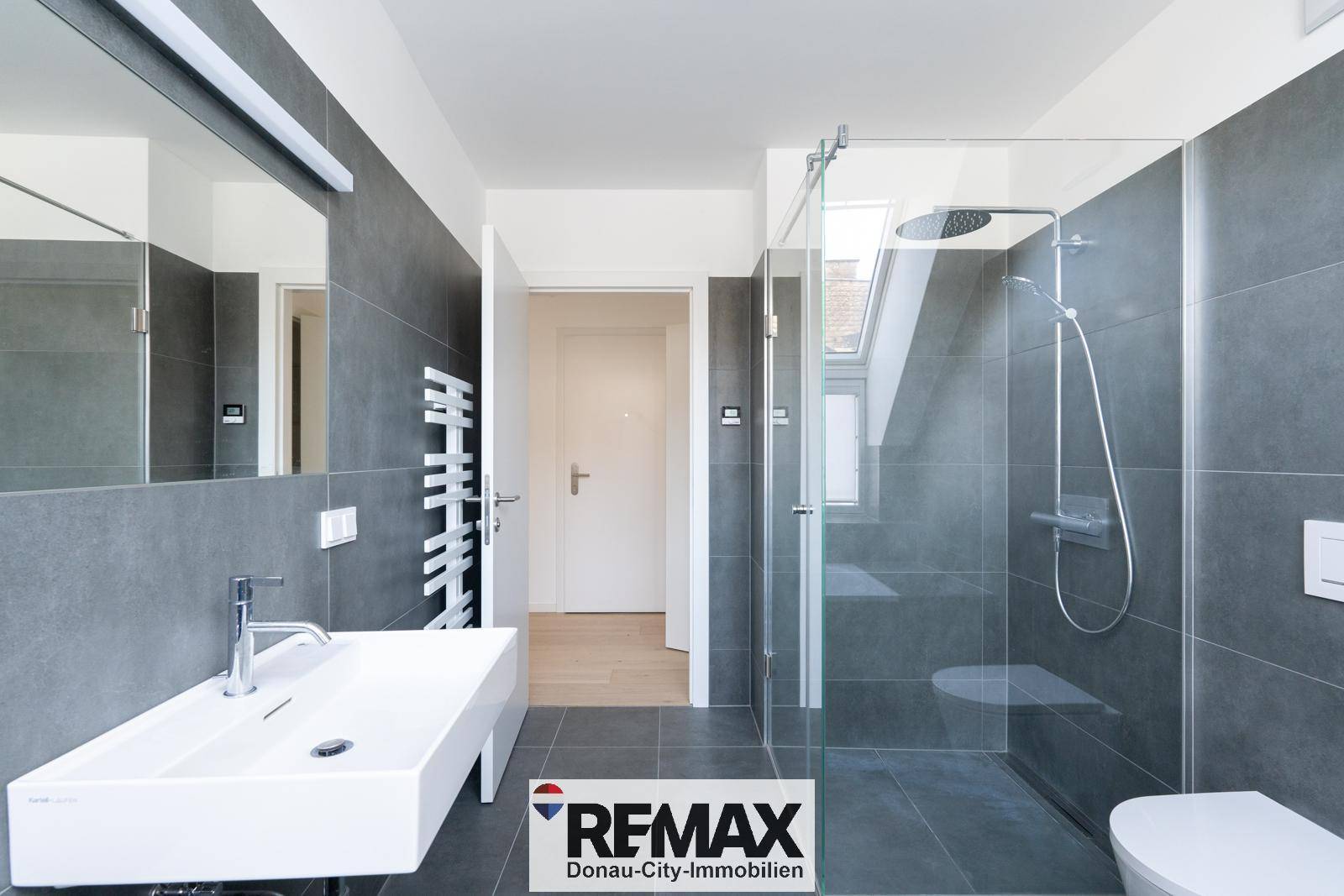 Modernes Badezimmer mit begehbarer Dusche, Einzelwaschbecken und grauen Fliesen.