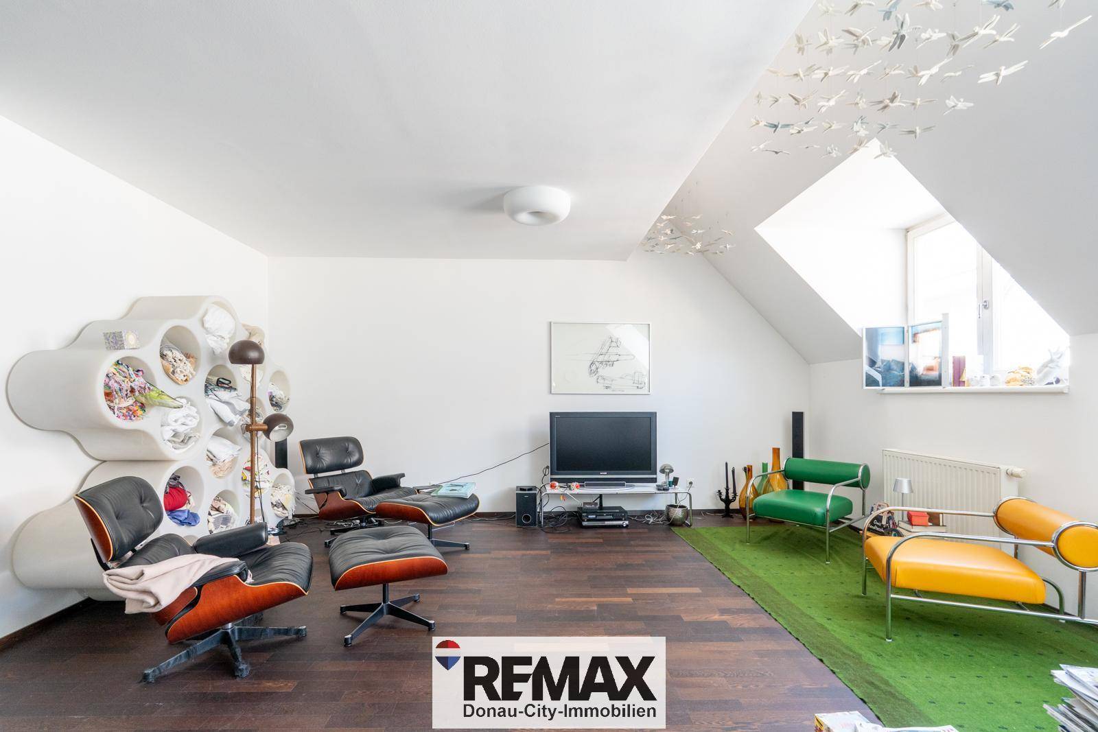 Gemütliches Wohnzimmer im Dachgeschoss mit dunklem Holzboden, Designermöbeln und Dachfenster.