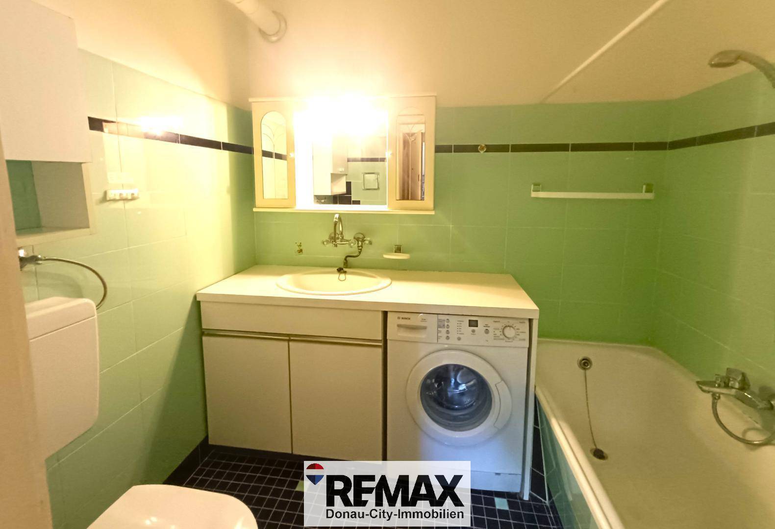 Badezimmer mit grünen Fliesen, Badewanne und einer Waschmaschine.