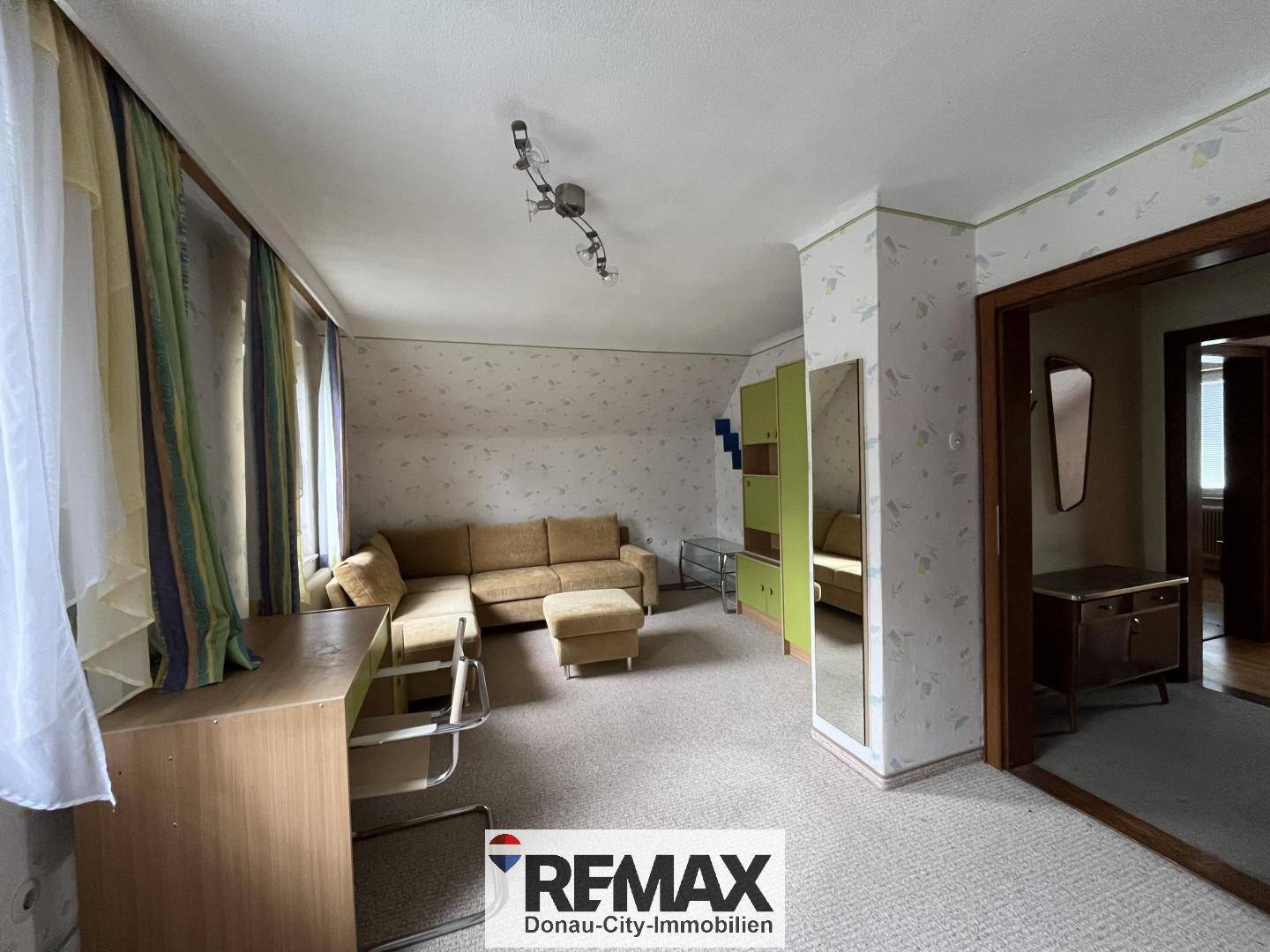 Geräumiger Wohnbereich mit Sofa, Teppichboden und gemusterter Tapete, mit viel Tageslicht.