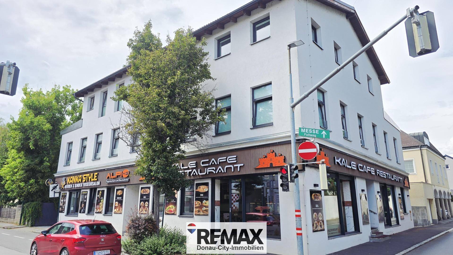 Eckansicht des Gebäudes mit Restaurant, umgeben von städtischer Infrastruktur und Grünflächen.