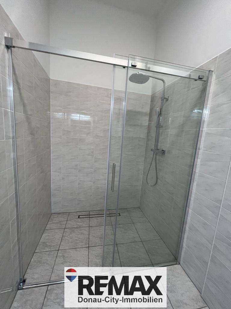 Geräumige Duschkabine mit Glaswänden und Regendusche in einem gefliesten Badezimmer.
