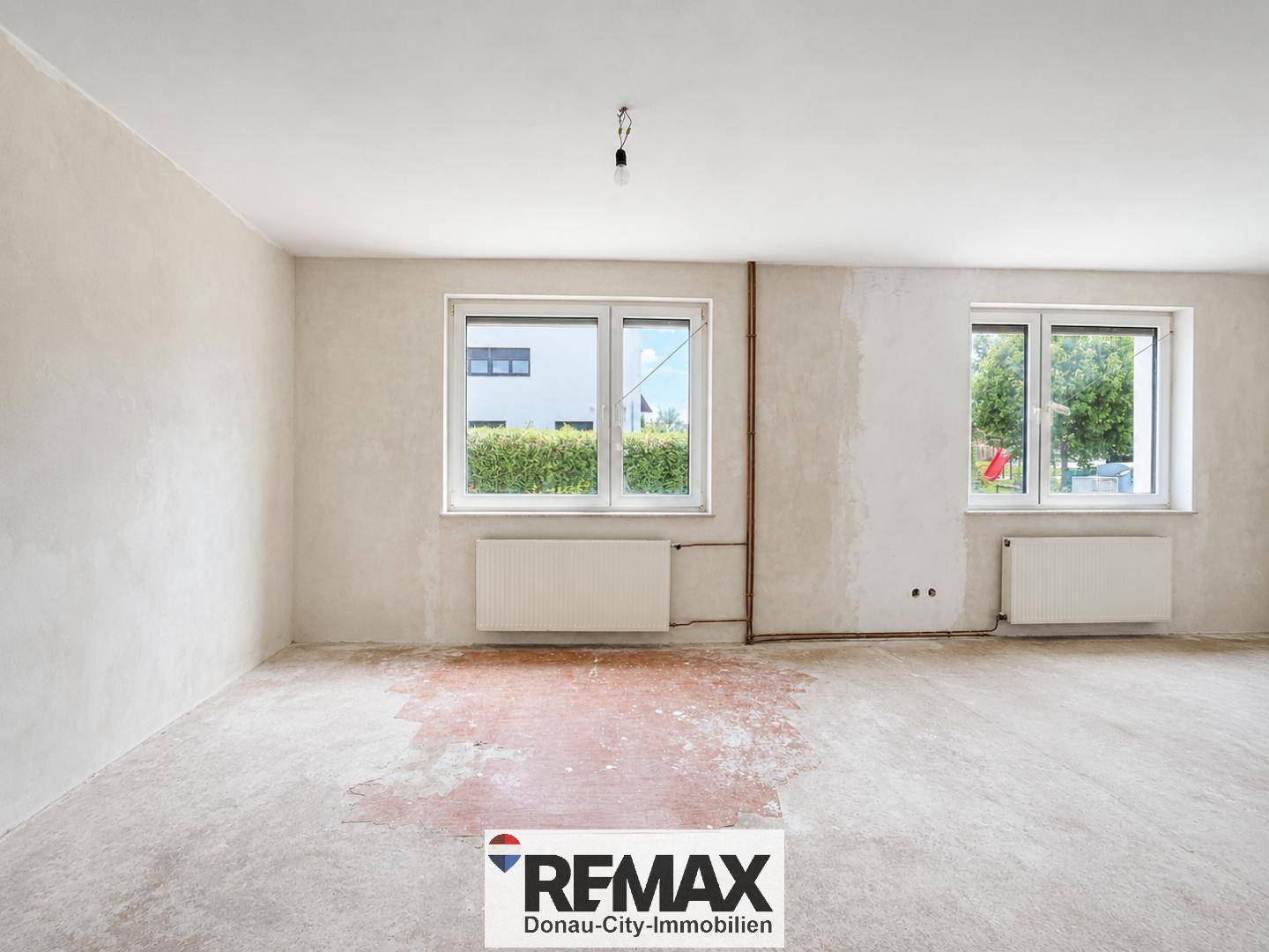 Großer Raum in Renovierung mit zwei Fenstern und unfertigem Boden.