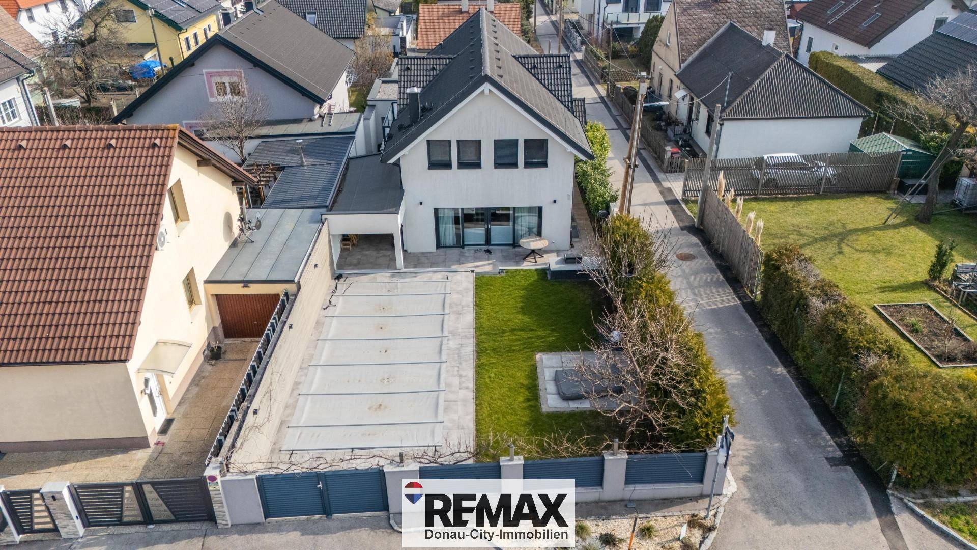 Luftaufnahme eines modernen Hauses mit Garten, Terrasse und umliegender Bebauung.