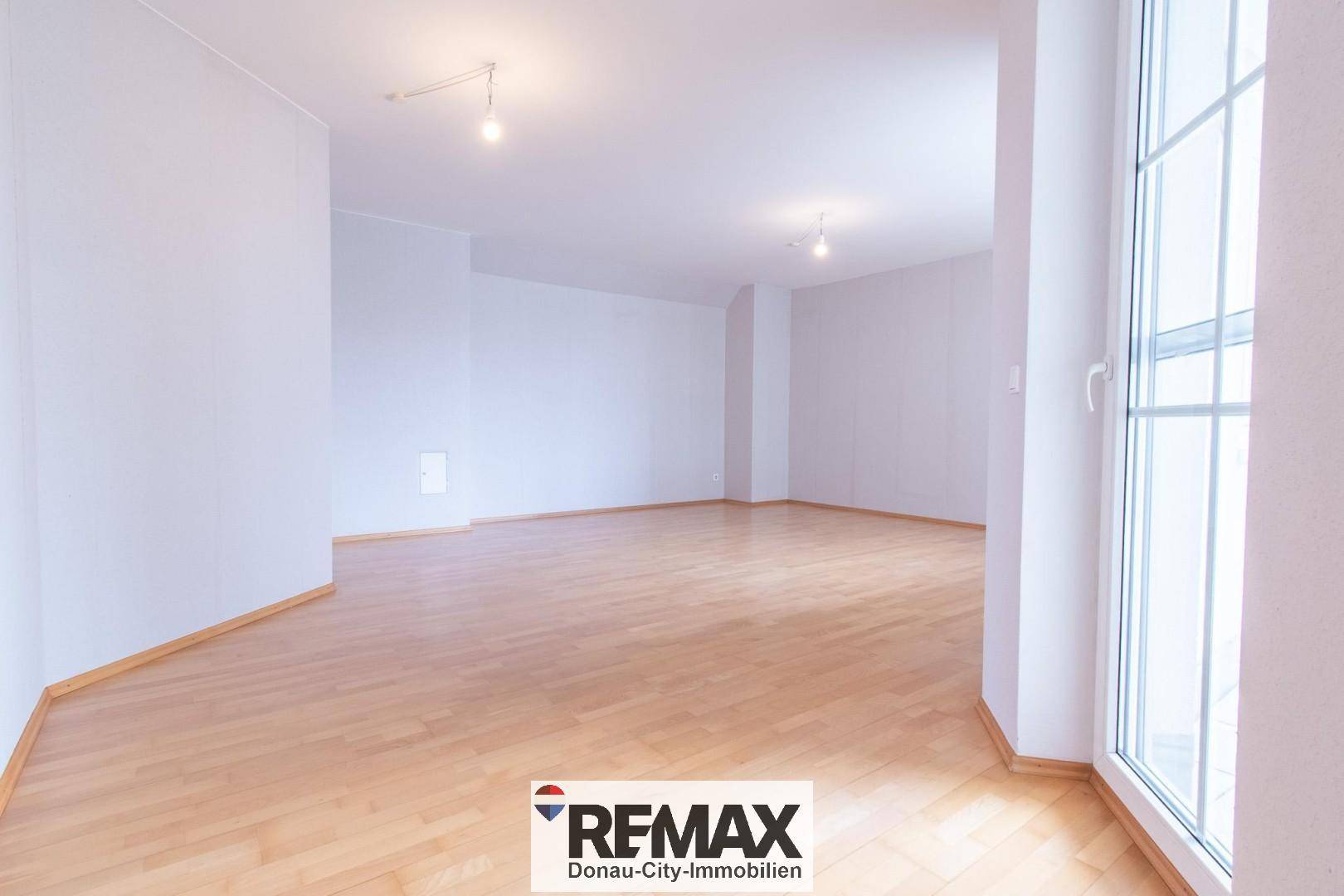 Heller, leerer Raum mit hellem Holzfußboden und großen Fenstern, ideal als Wohnzimmer.