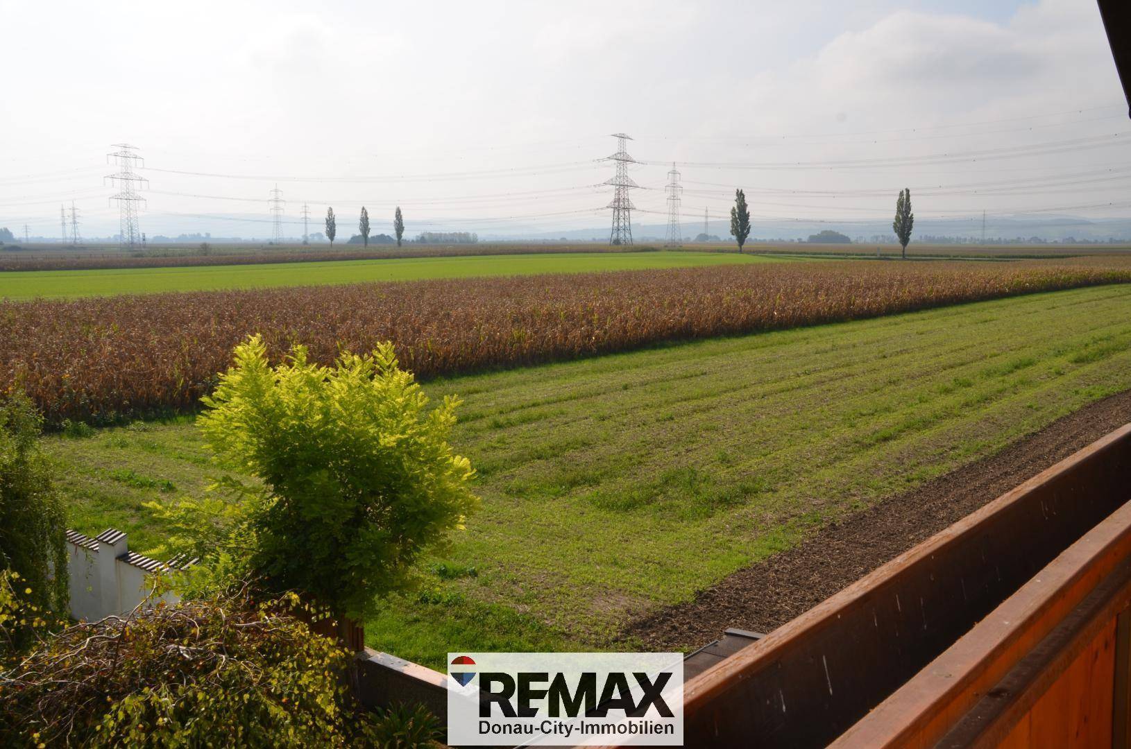 Weitläufiger Blick über Felder und ländliche Landschaft mit Stromleitungen am Horizont.