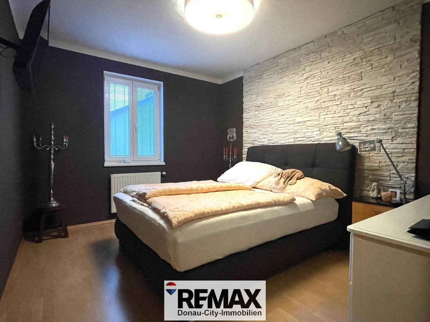 Schlafzimmer mit Doppelbett, dunklen Wänden und dekorativer Steinwand.