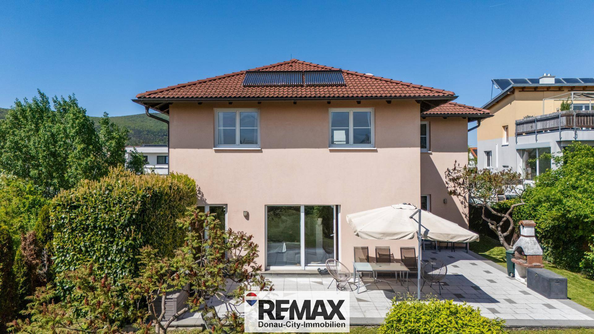 Rückseite des Hauses mit sonniger Terrasse, Grillbereich und Photovoltaikanlage auf dem Dach.