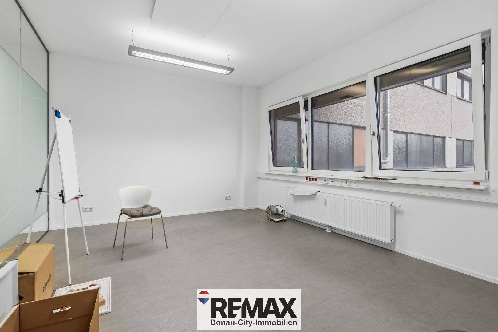 Helles Büro mit großen Fenstern, Heizkörper und einer weißen Tafel.