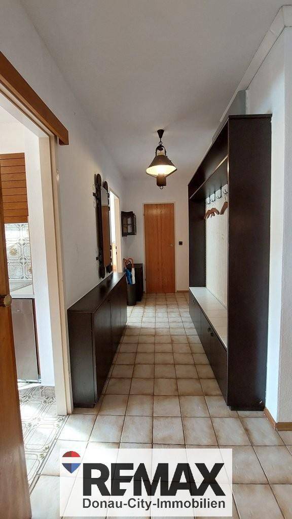 Langer Flur mit Fliesenboden, Garderobe und Blick auf die Eingangstür.