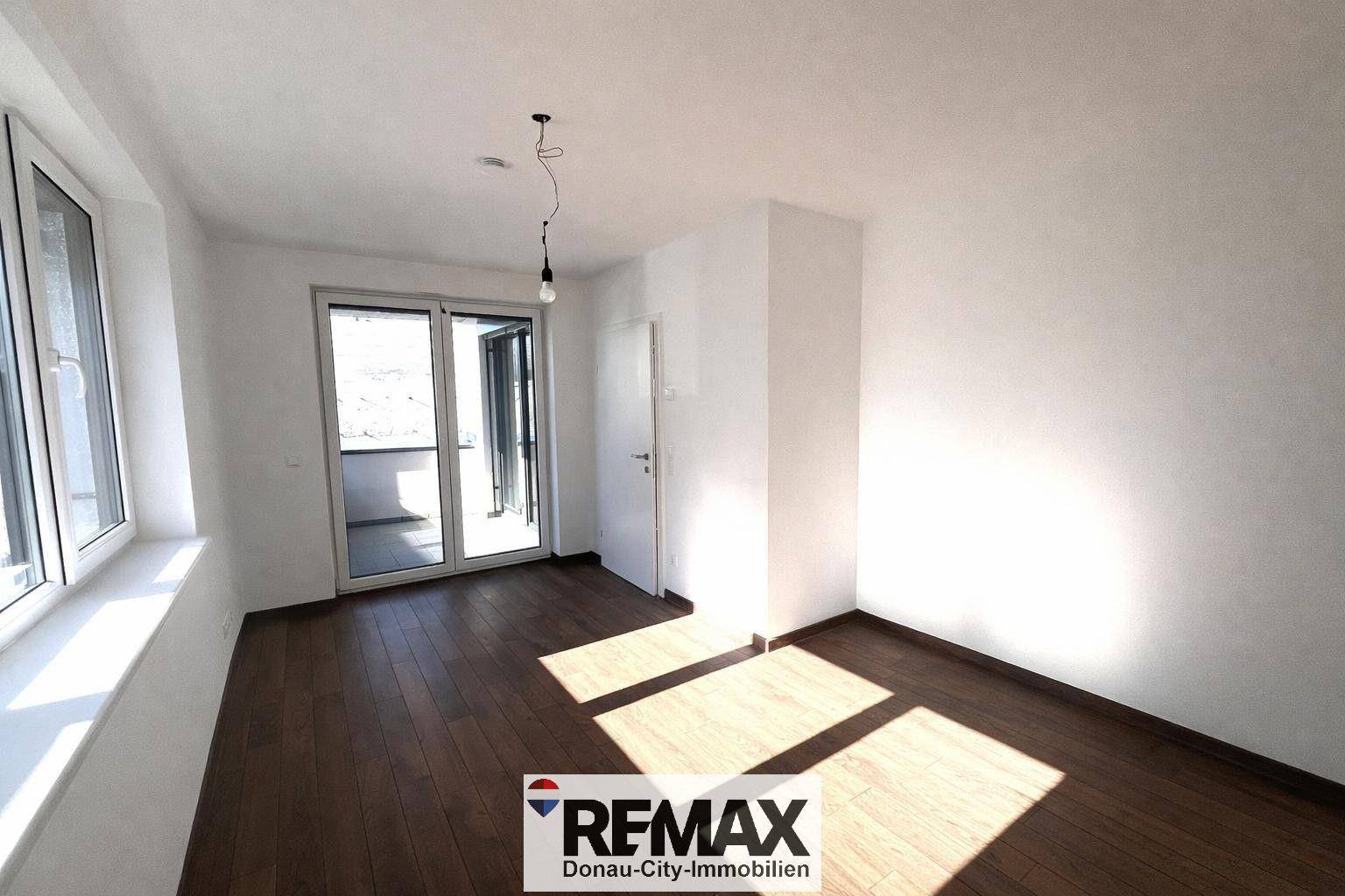 Helles Zimmer mit dunklem Holzboden und Zugang zu einem Außenbereich, ideal als Schlafzimmer.