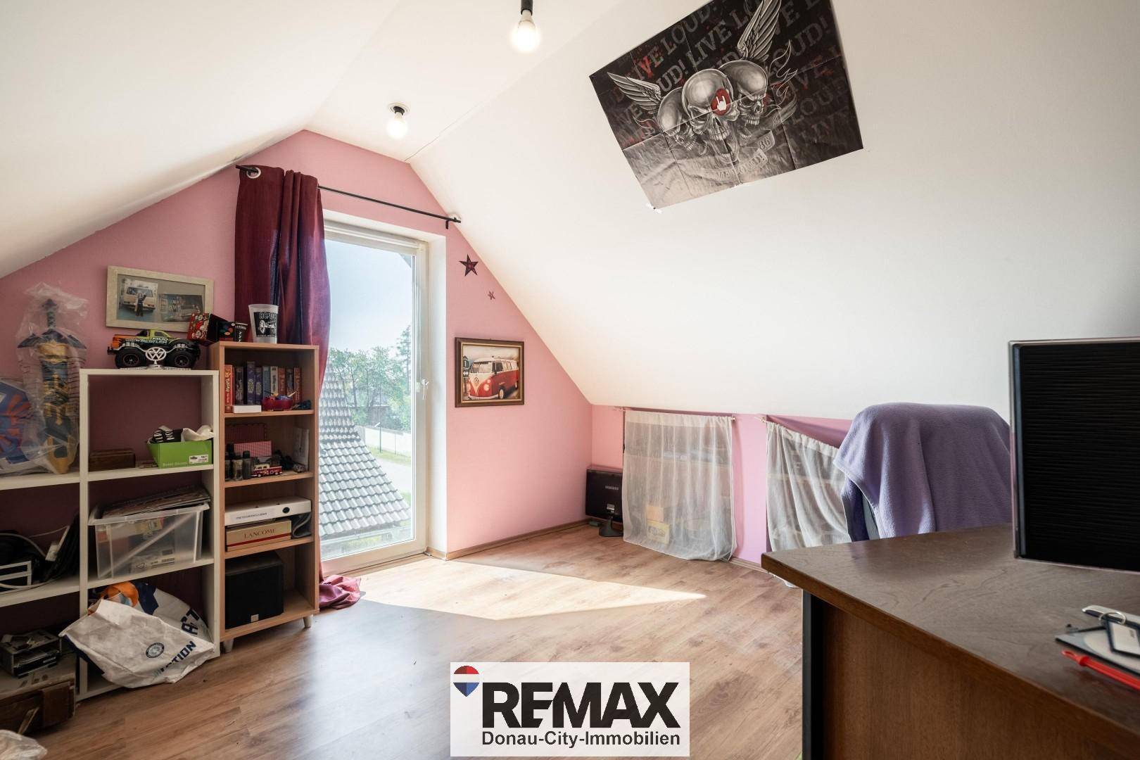Dachzimmer mit schräger Decke, rosa Wand und großem Fenster für viel Tageslicht.