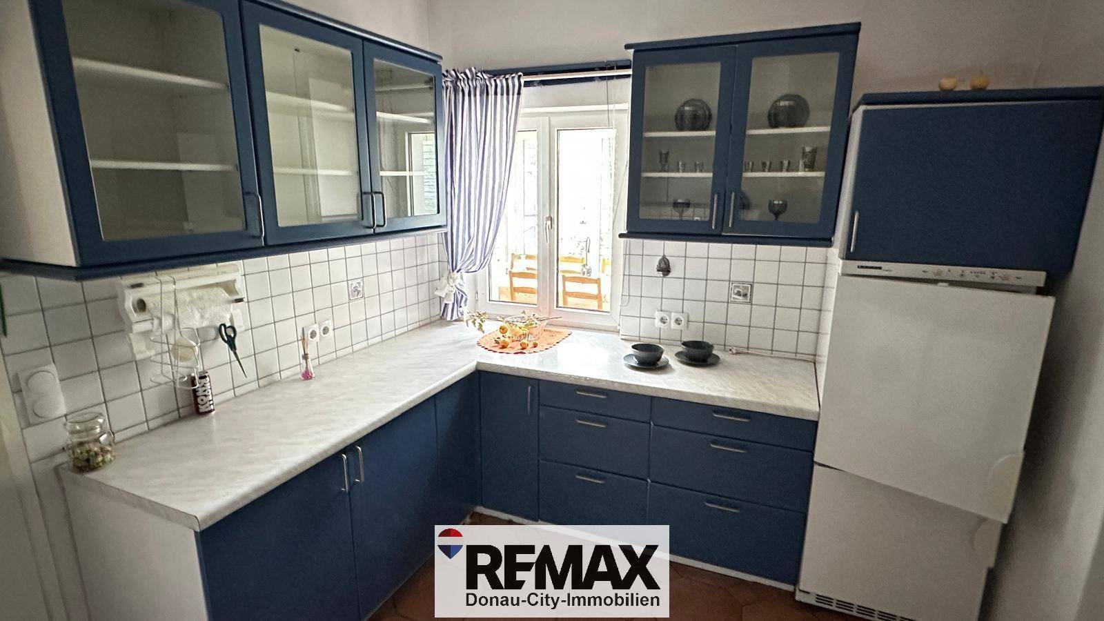 Küche mit blauen Schränken, weißen Fliesen und einem Fenster für Tageslicht.