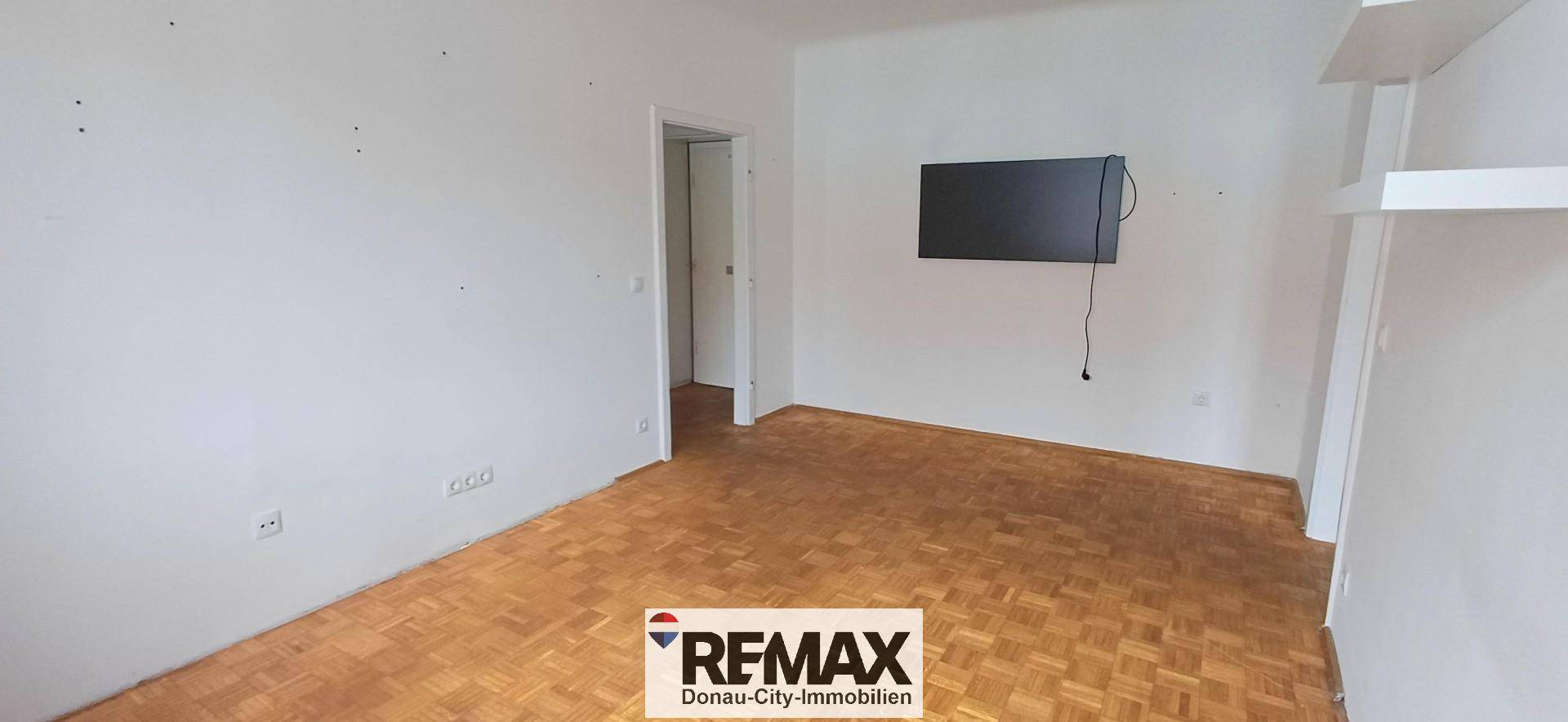 Geräumiges Zimmer mit Parkettboden und einer Wandhalterung für einen Fernseher.