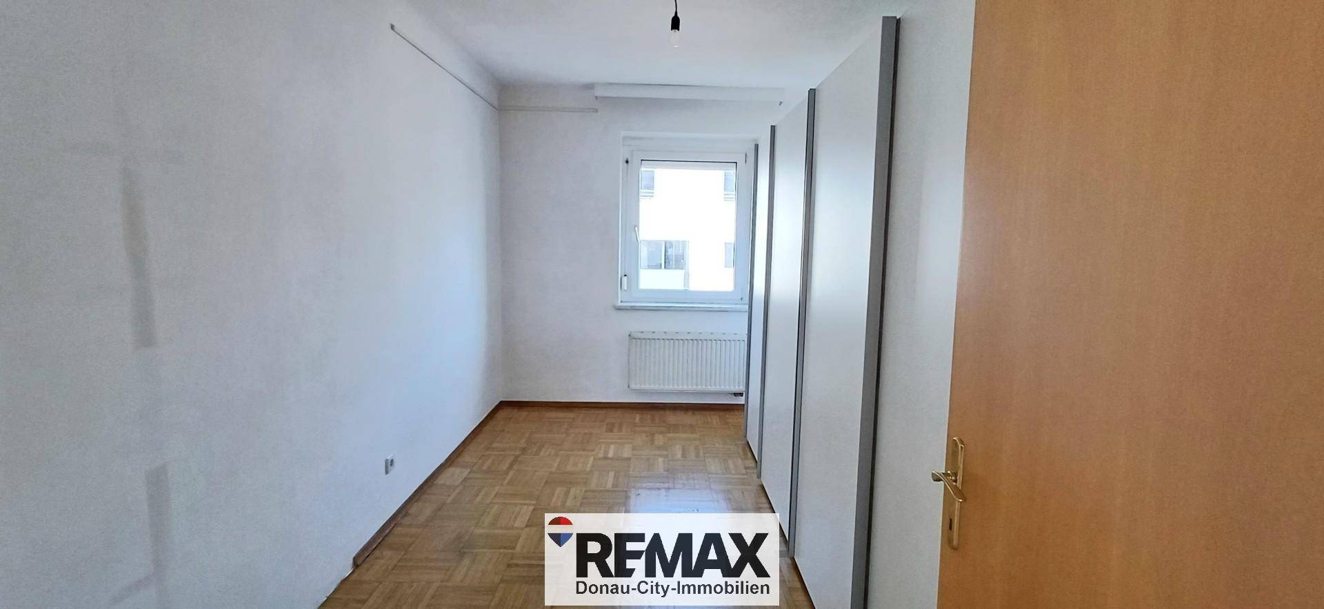 Helles Schlafzimmer mit Parkettboden und einem Fenster, das viel Tageslicht hereinlässt.