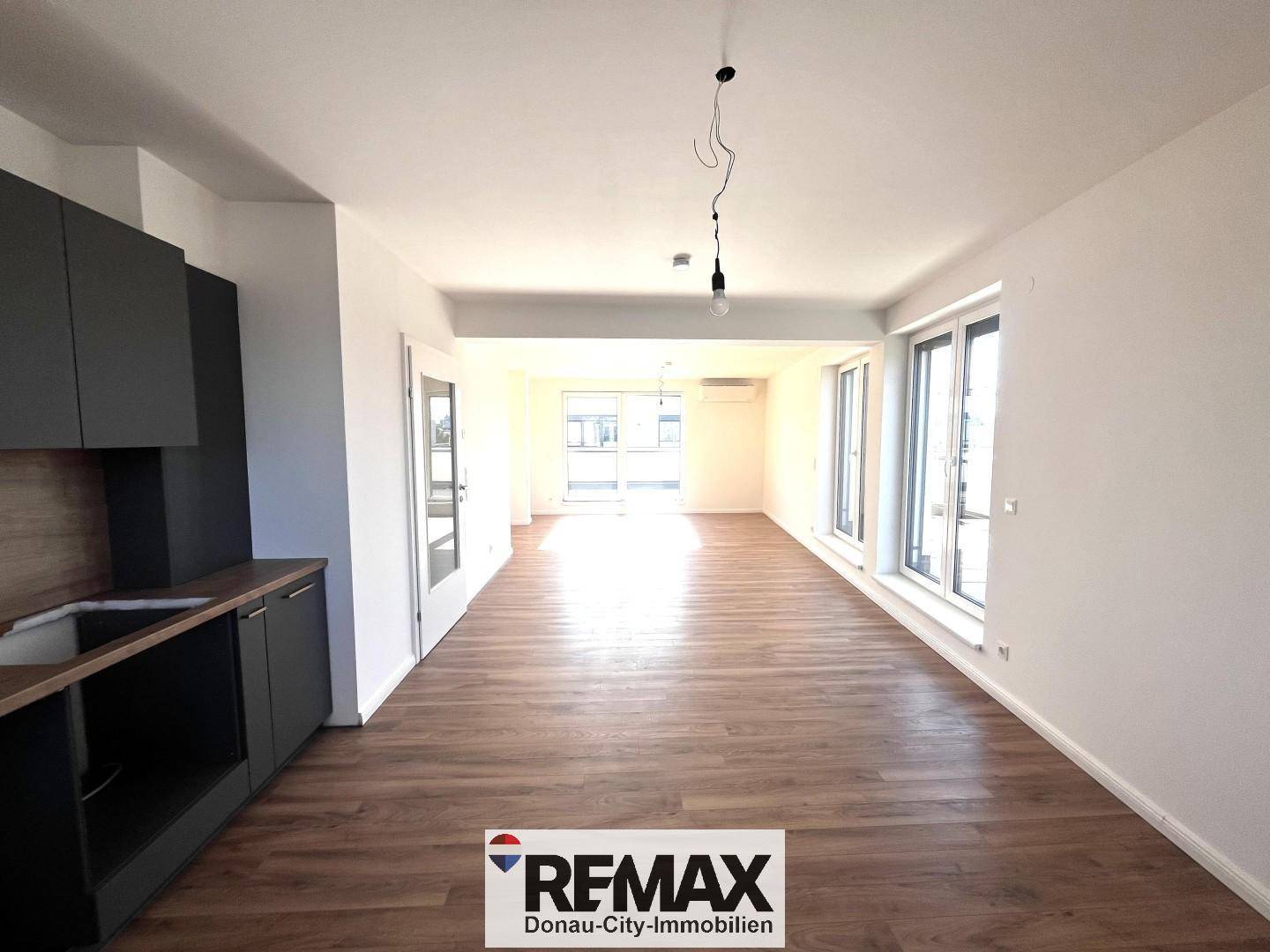 Geräumiger, offener Wohnbereich mit Holzboden und viel Tageslicht durch große Fenster.