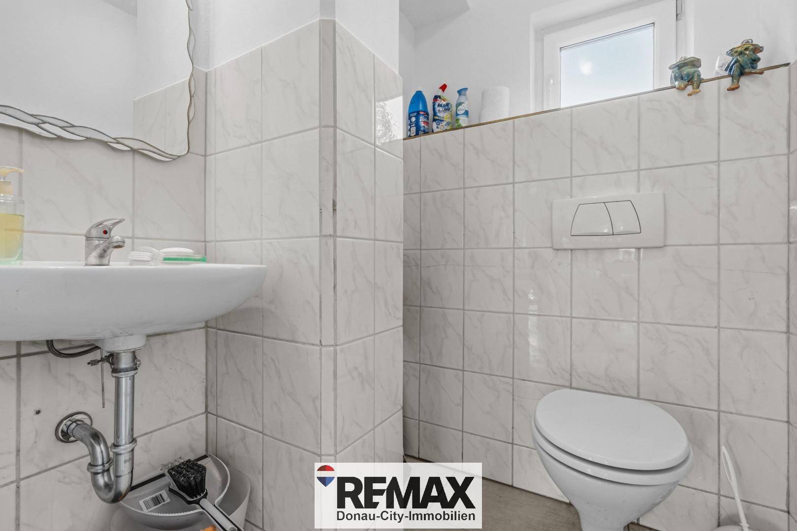 Kleines WC mit weißen Fliesen, wandmontierter Toilette und Fenster.