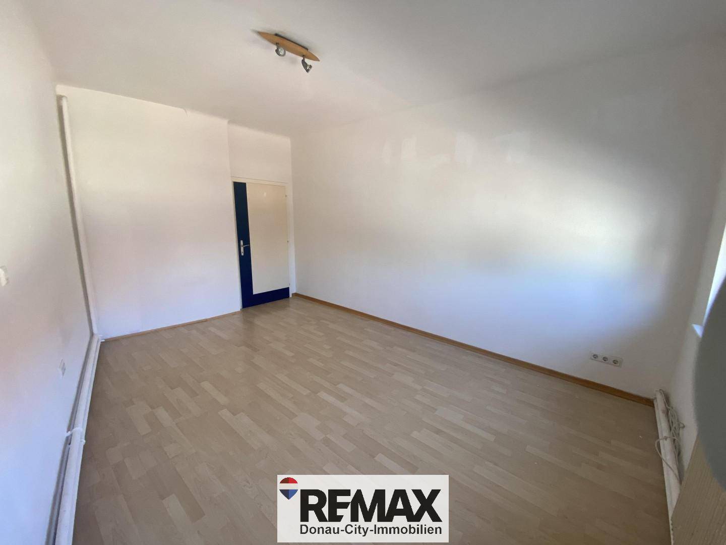 Leeres Wohnzimmer mit hellem Laminatboden und weiß gestrichenen Wänden, bereit zur Einrichtung.