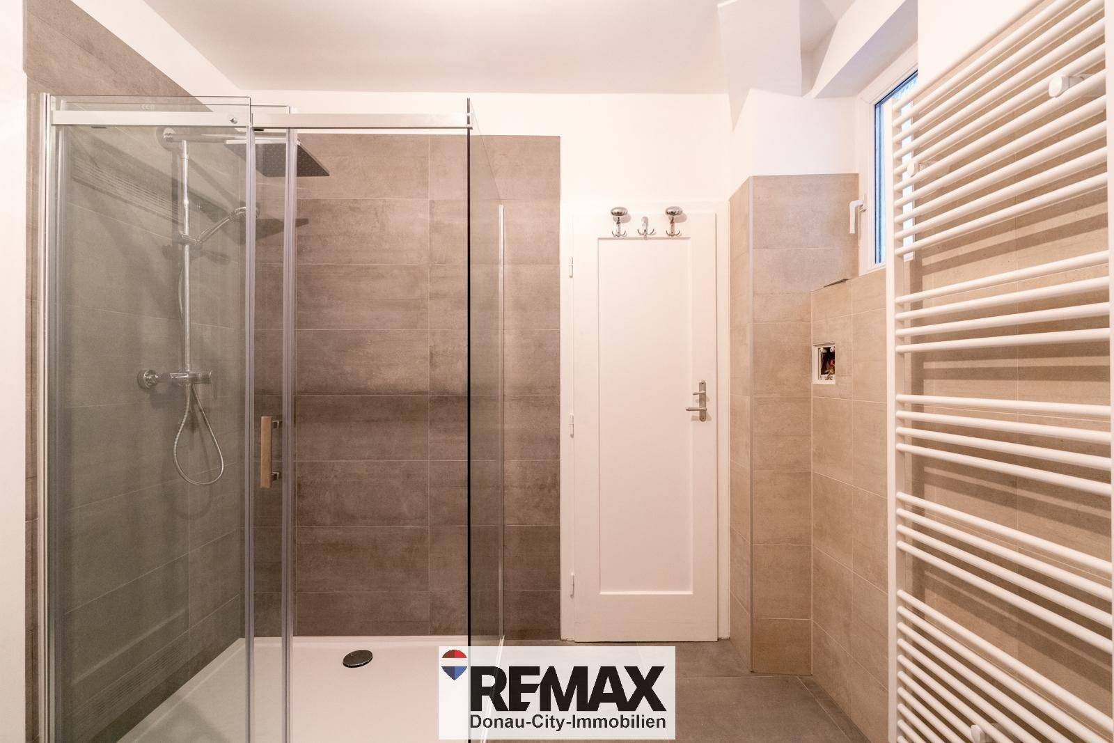Modernes Badezimmer mit großer Glasdusche, beigefarbenen Fliesen und Handtuchheizkörper.