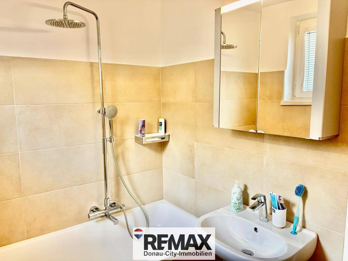 Badezimmer mit Badewanne, Duscharmatur und Spiegelschrank über dem Waschbecken.