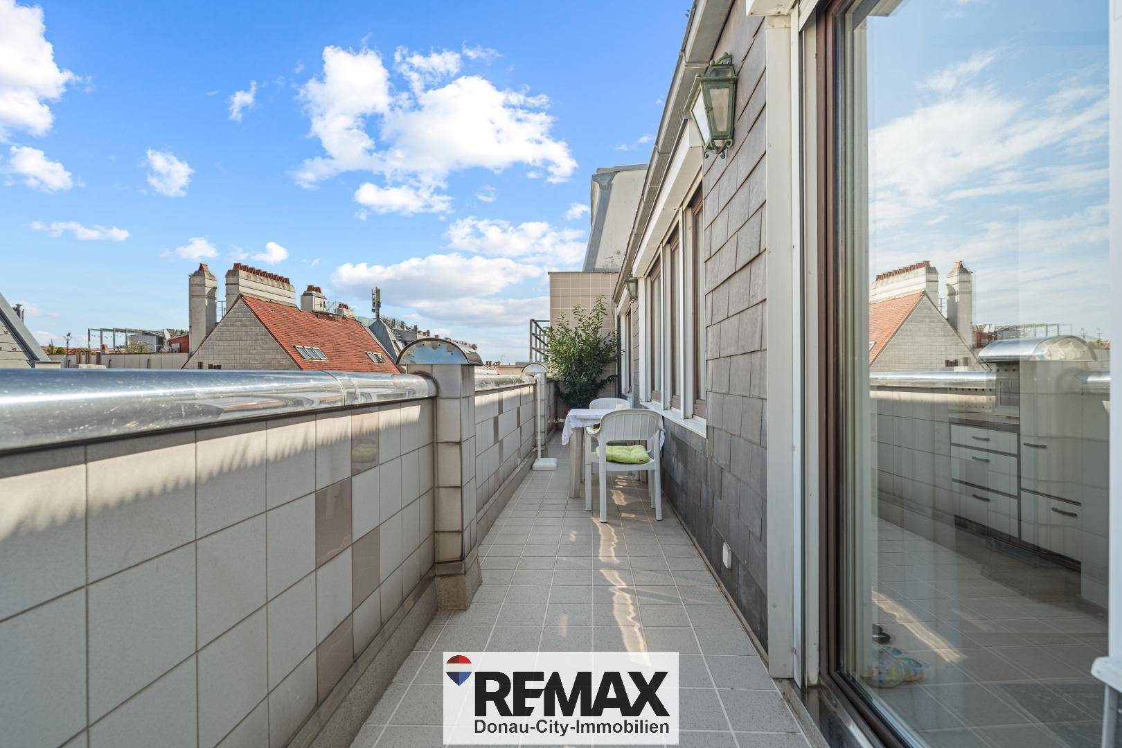 Langer, schmaler Balkon mit Fliesenboden und Sitzgelegenheiten, mit Blick auf die Stadt.