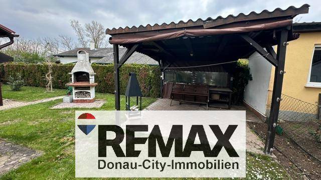 Überdachter Sitzbereich im Garten mit Grillplatz und Rasenfläche.