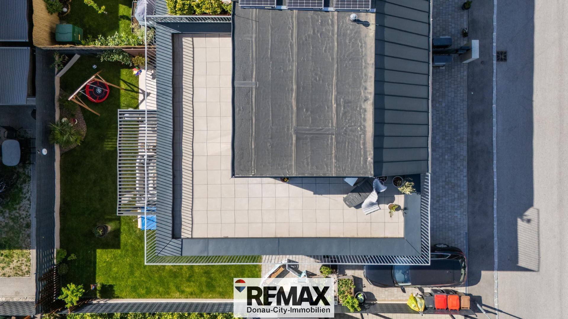 Draufsicht auf das Haus mit Flachdach, Photovoltaikanlage, Garten und Parkplatz.