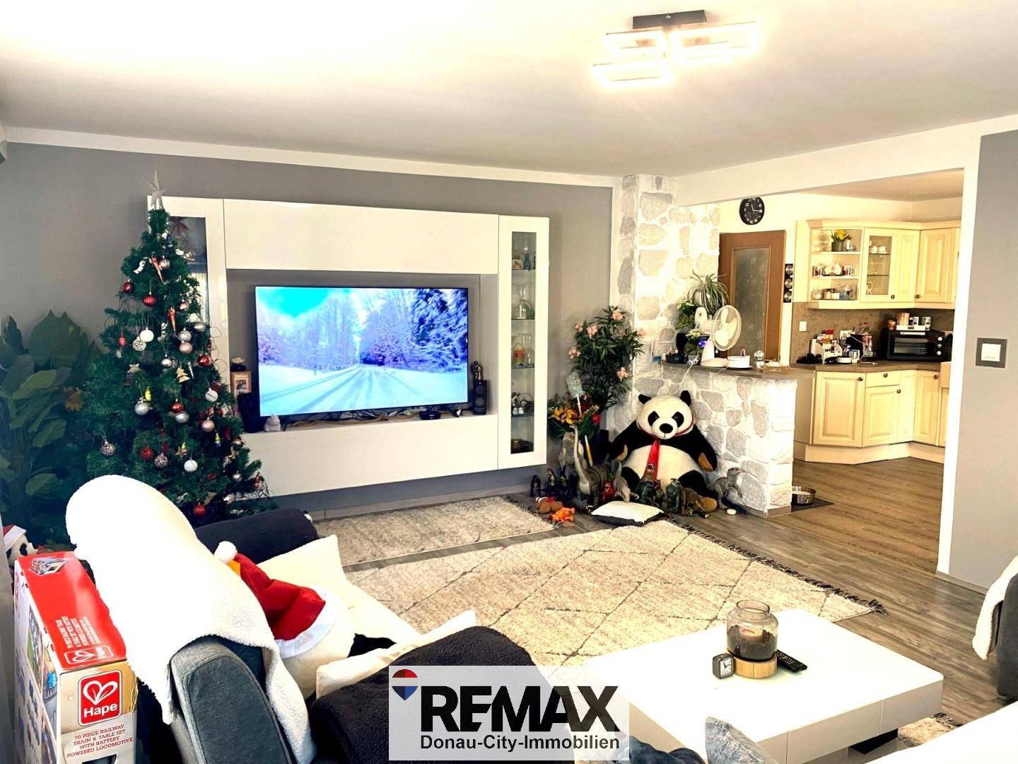 Gemütliches Wohnzimmer mit großem Fernseher und Blick auf die offene Küche im Hintergrund.