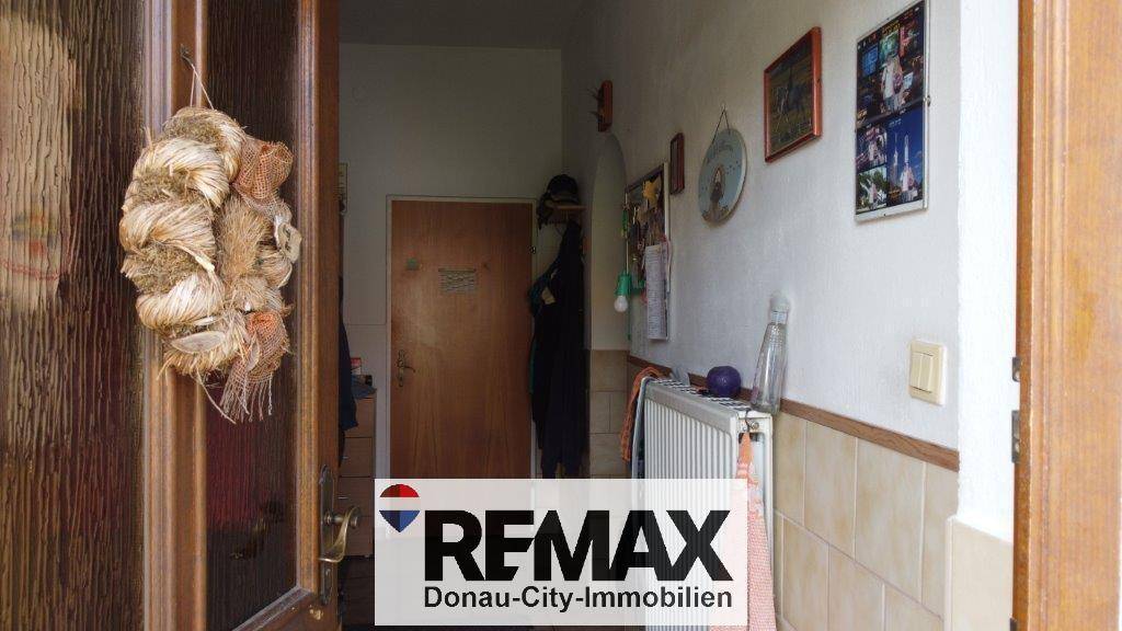 Eingangsbereich oder Flur mit Fliesenboden, Heizkörper und einer Holztür, die in den Innenraum führt.