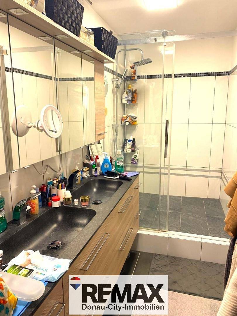 Modernes Badezimmer mit Doppelwaschbecken, großer Duschkabine und hellen Fliesen.